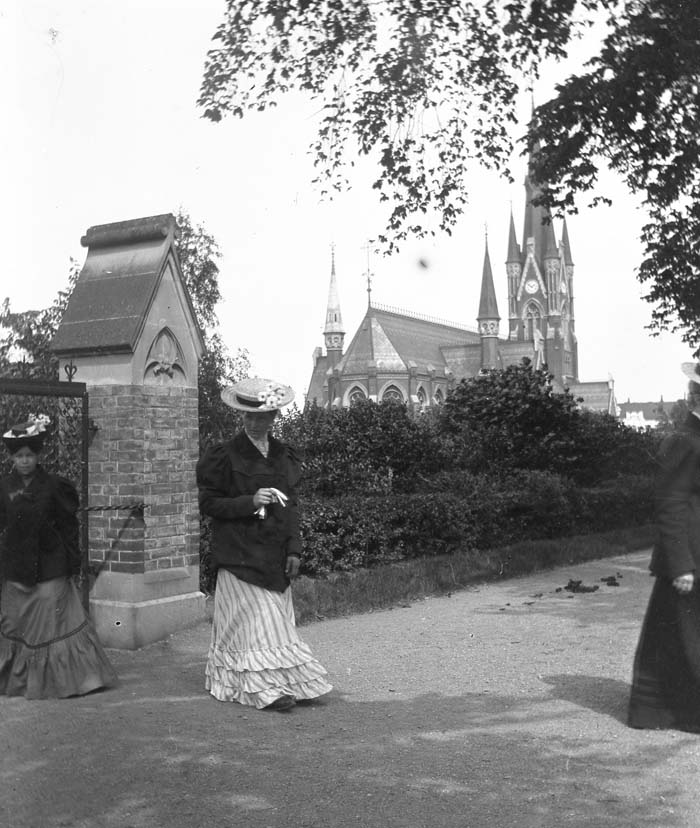 En kvinna framför en grindstolpe. I bakgrunden Matteuskyrkan i Norrköping.