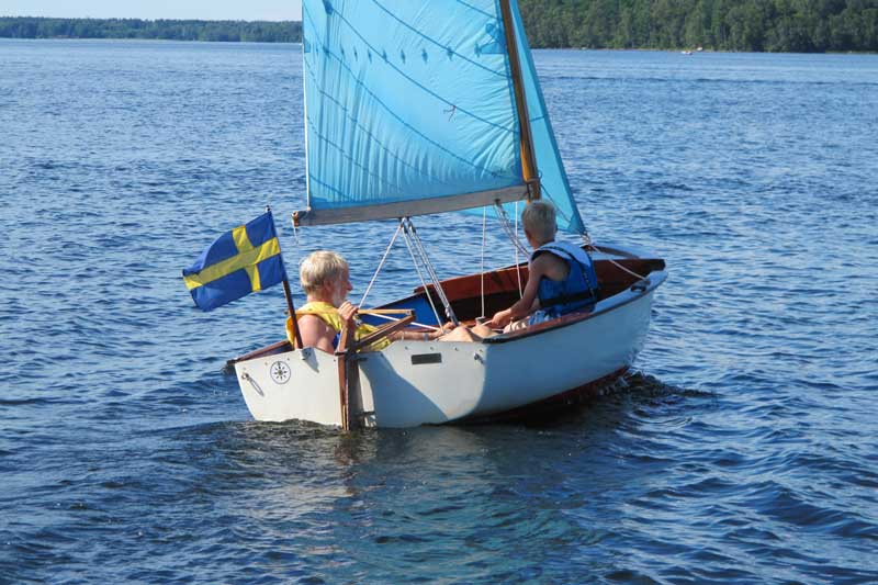 Man och pojke i en liten segelbåt på sjön. Solsken.