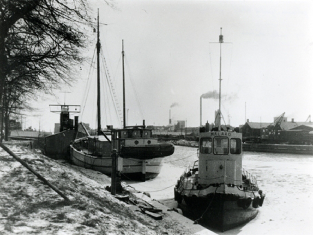 Mälarö är en liten bogserbåt med styrhytt midskepps och mantåg längs relingen. Hon har däck hängandes längs med skrovet som fendrar. På den svartvita bilden ligger fartyget i Köpings hamn. 