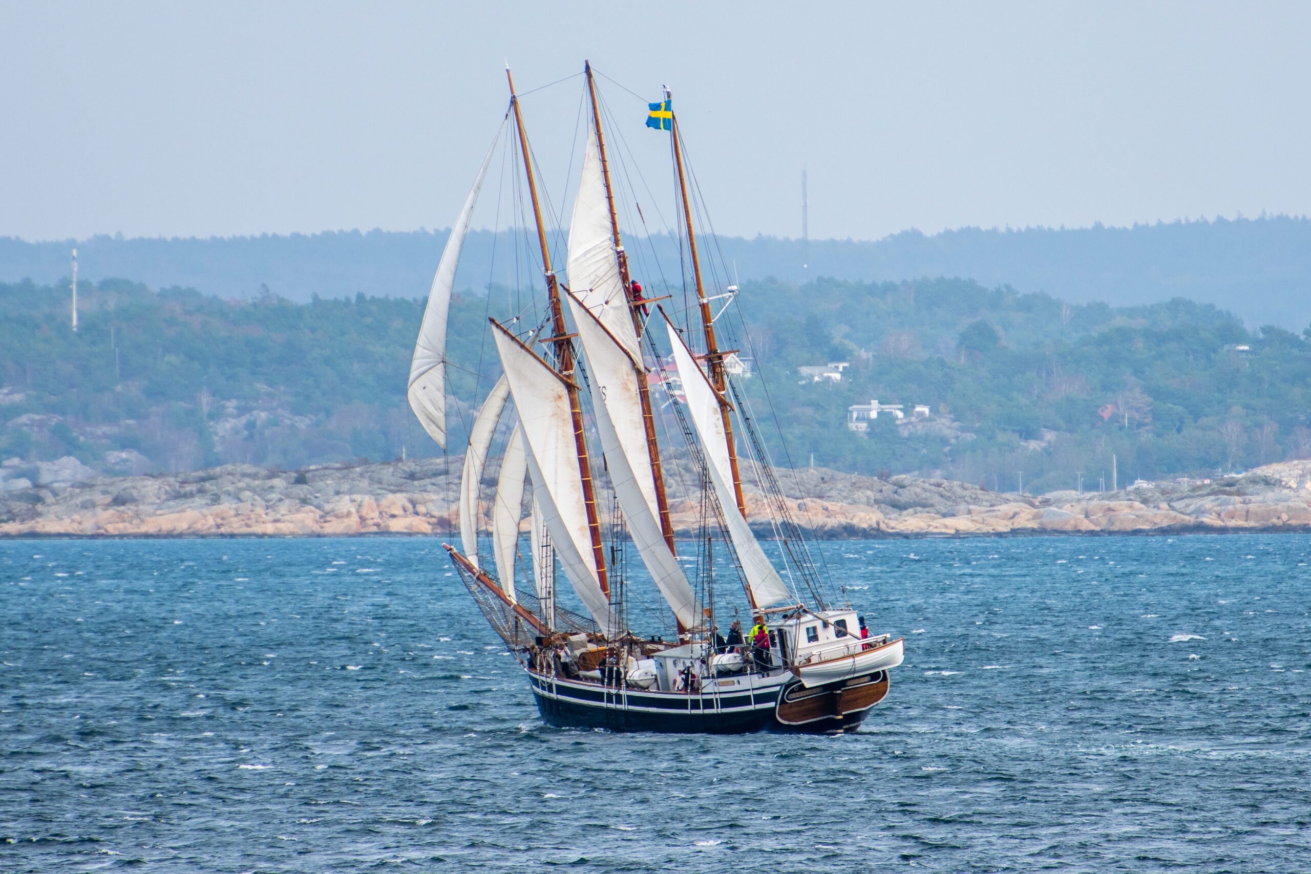 Westkust är ett tremastat segelfartyg. Hon går för fulla segel utanför Orust kust. Hon har en styrhytt i aktern och över akterspegeln hänger en livräddningsbåt.