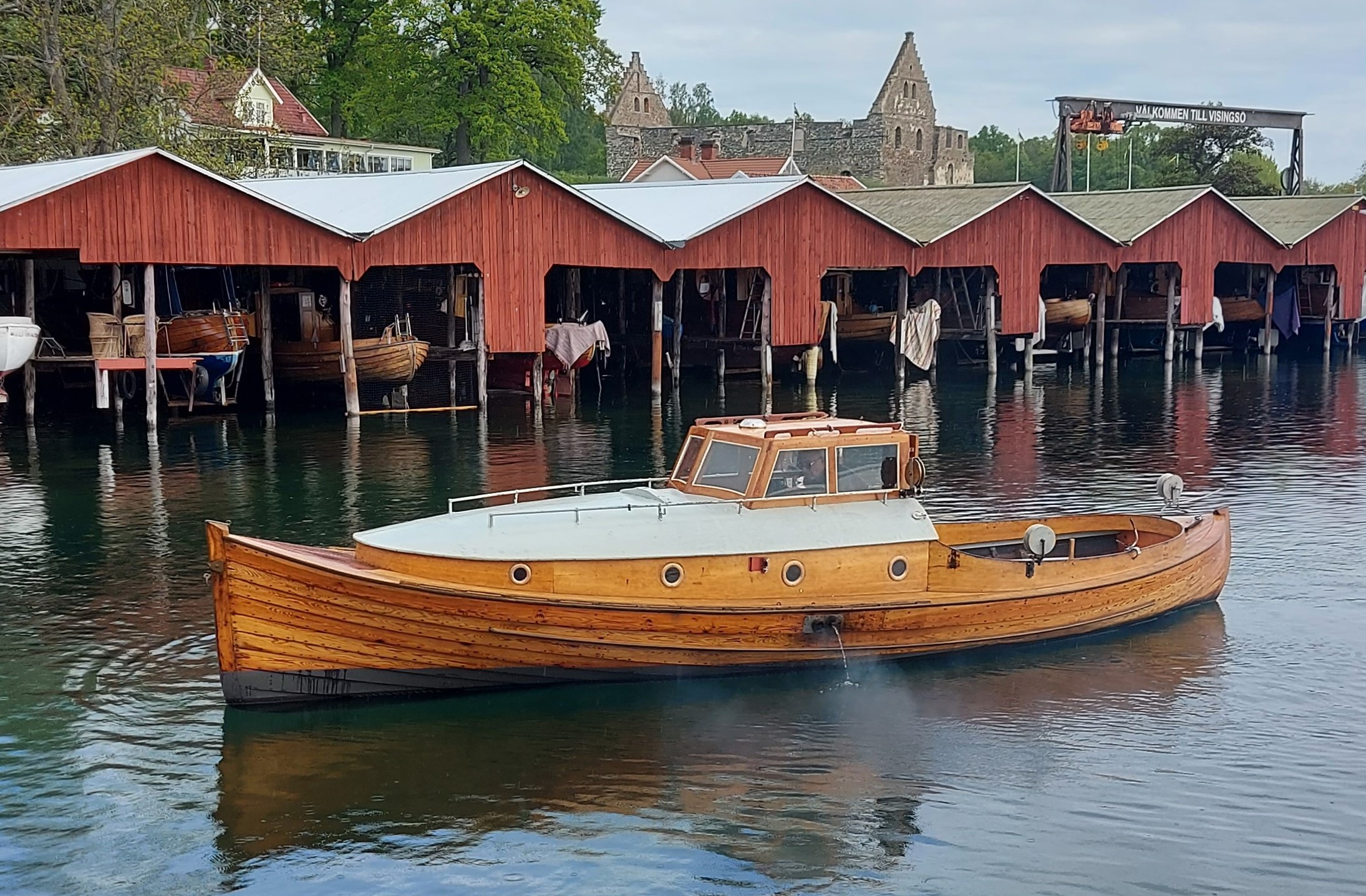 Advokatbåten är en traditionell fiskebåt med klinkbyggt träskrov. Den har en förruff med fyra ventiler, en sittbrunn i aktern och en styrhytt. Bakom båten syns båthus på rad.