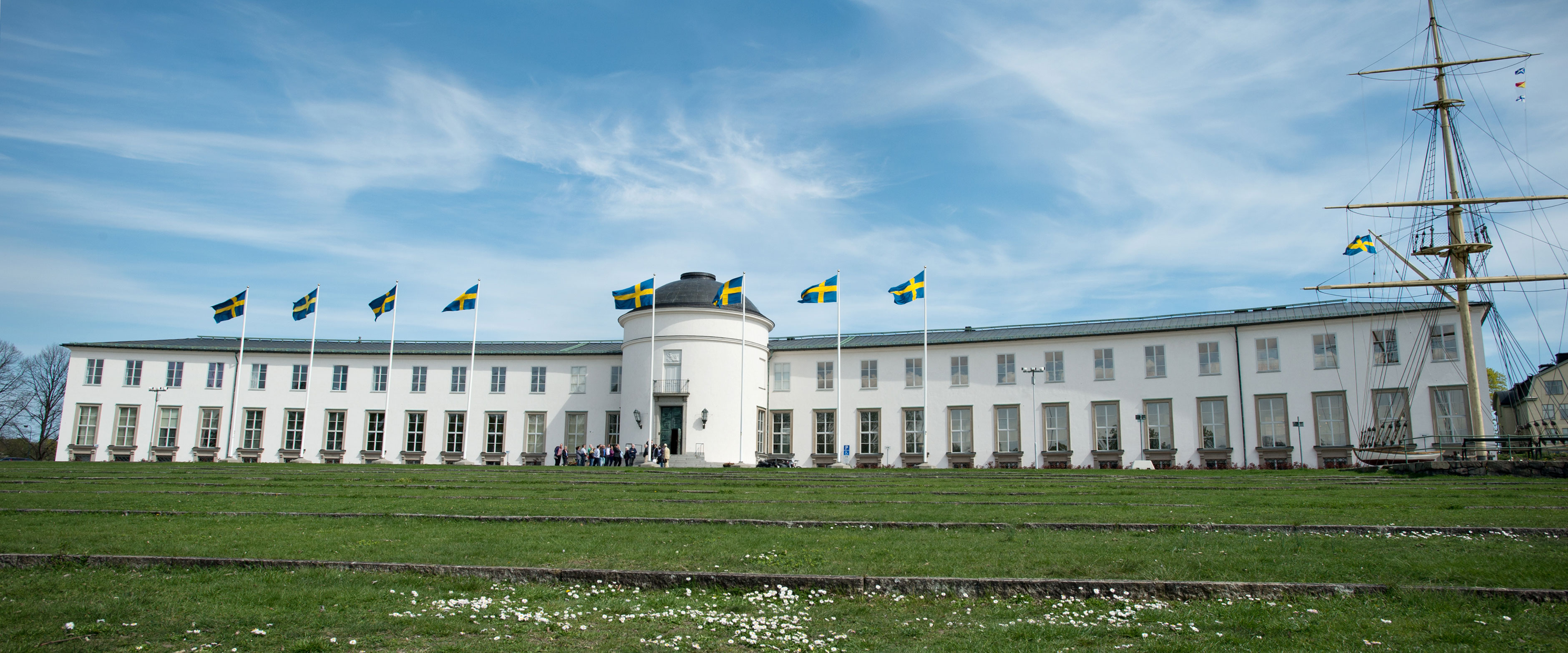 Ett stort vitt hus med många förnster på en grön gräsmatta. Huset är Sjöhistoriska museet.